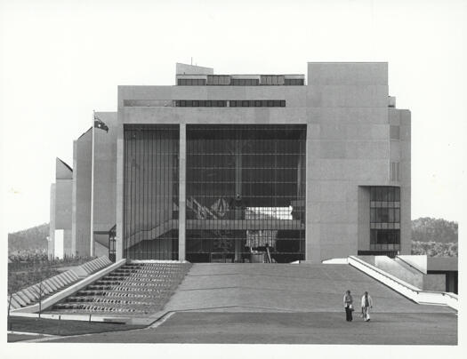 Front view of the High Court of Australia, Parkes. Two people walking across the forecourt.