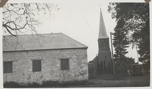 Western side of St John's Schoolhouse, Reid with the Anglican Church of St John the Baptist in the background. A car is parked nearby.