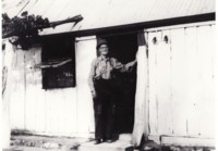 House built by Thomas Tong showing his son Jack in the doorway. The house was built with wooden slabs and has a tin roof.