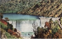 Text on the back: Picturesque Cotter Dam, shows water cascading over the wall. Cotter Dam is the source of Canberra's water supply. Capacity 380,000,000 gallons with a safe draught of 7,000,000 gallons daily. Autumn season.