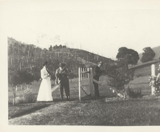 John Gale at the gate to his property. A man and a woman (both unnamed) are also in the photo.