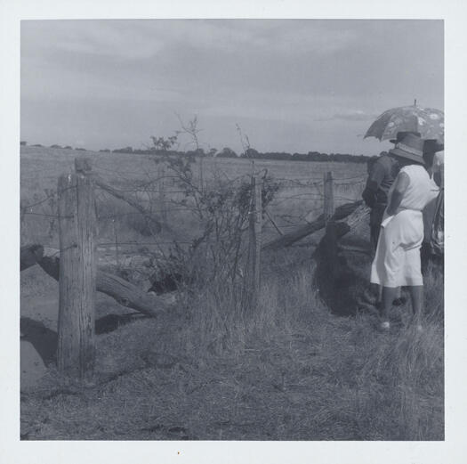 Photo shows at least 4 people standing beside a fence looking across an open paddock near Gundaroo.