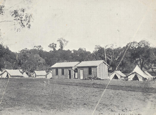 Survey camp on Capital Hill. Shows tents and two timber buildings against a background of trees.