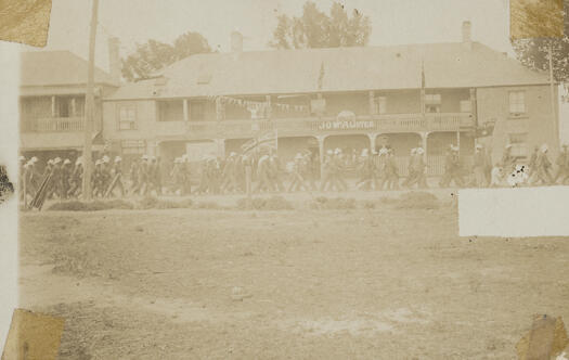 J.O. McAlister's shop, Bungendore. Large group marching past - possibly Boer War recruitment.