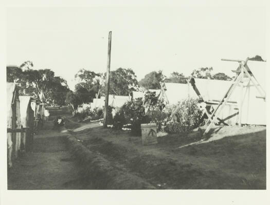 Tents occupied by builders with flowers growing in small gardens at the front of the tents outlined by white-painted rocks.