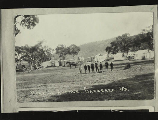 A view of eight children in the middle distance. A horse and cart is in front of some buildings (possibly houses).