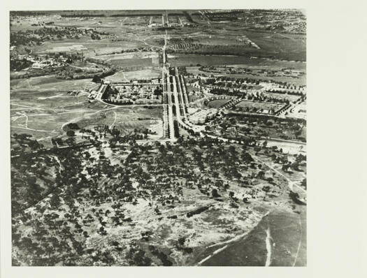 Aerial view of Commonwealth Avenue with a part view of Parliament House, Hotel Canberra, West Block, and across the river the Sydney and Melbourne Buildings