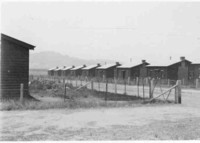 Construction camp at the Causeway, showing a line of eight wooden cubicle-type houses on one side of a dirt road. Mount Ainslie is in the background.