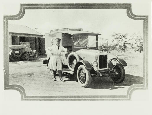 Early model Canberra ambulance with the driver standing beside the vehicle.