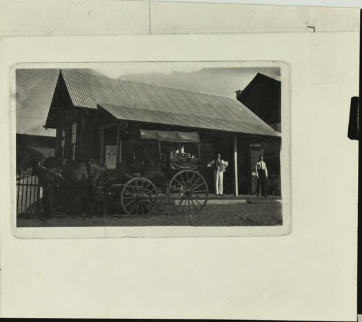 Horse-drawn delivery to the Railway Station with two men standing in front of the station