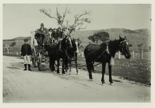 A team of three horses pulling a wagon with at least five children and a driver. The children are from the Cotter. A policeman is standing beside the wagon.