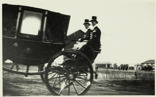 Funeral carriage showing two men in livery with top hat on the back of a wagon.