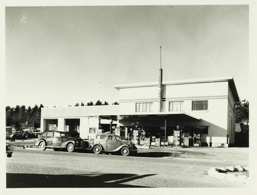 Front view of a Braddon garage. Shows two cars parked at the kerb and petrol bowsers. Street address unknown.