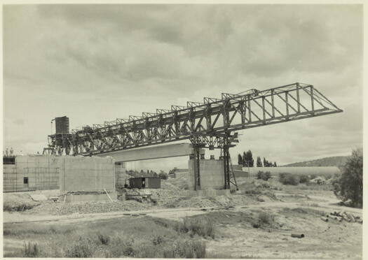 Kings Avenue Bridge under construction. Shows an angled view to the west of a pre-stressed concrete beam in position after being lowered from the steel gantry.