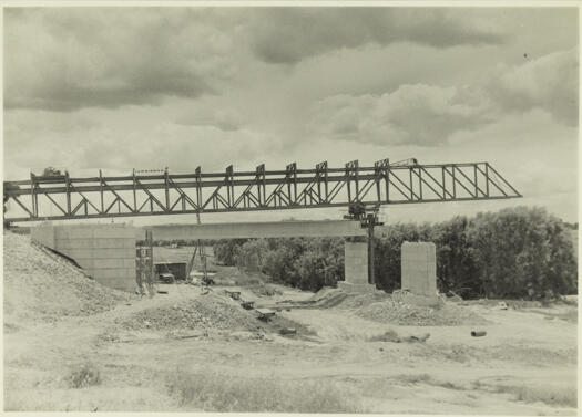 Kings Avenue Bridge under construction. A view looking west showing a pre-stressed concrete beam in position after being lowered from a gantry.