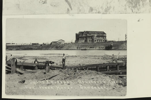 Shows the Power House in the background with a reservoir, being built to supply water to the Power House, in the foreground.