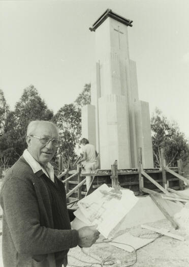 A view of a partly constructed church in Hackett, also showing a close view of a man looking at plans.