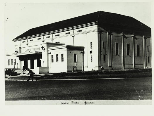 A front view of the Capitol Theatre, Manuka. It shows one man with a mattock outside the theatre and another working up the the steps of the theatre.