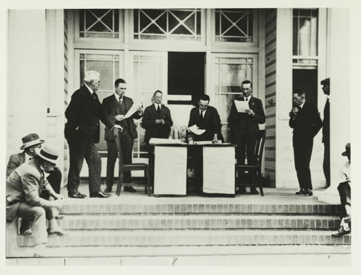 Land auction at the Manuka theatre site. It shows a desk on the steps and five men looking at papers.