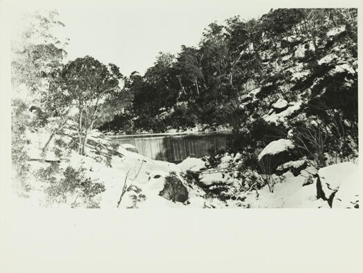 Cotter Dam in winter, 1913. The rocks are covered in snow.