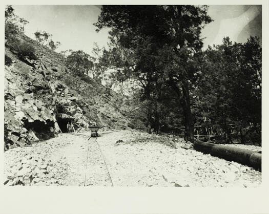 Cotter Dam tunnel. Photo shows a man standing in the entrance of the tunnel with a branch tram line going into the tunnel and a main line heading towards the dam.