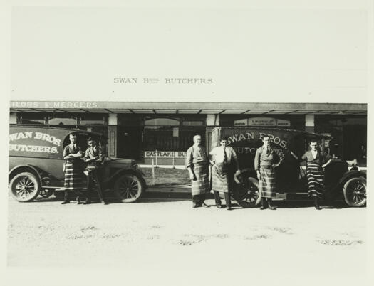 Swan butchery in Giles Street, Kingston. Six butchers are standing in front of two vehicles bearing the name Swan Bros Butchers.