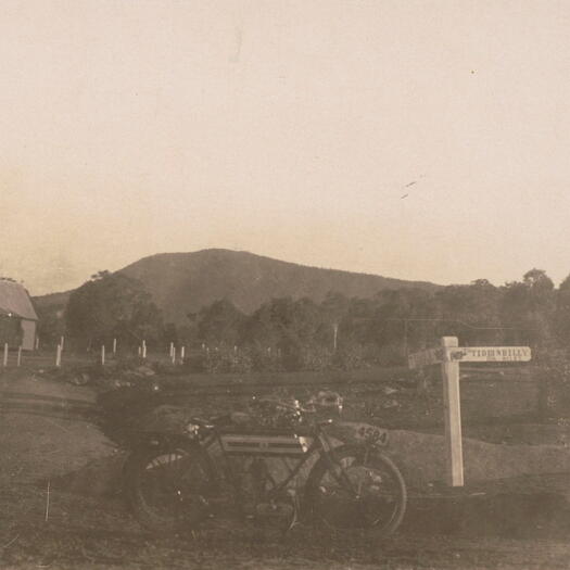 Signpost with motorcycle, Canberra to Tidbinbilly and Naas, taken at Tharwa with St Edmunds and Mt. Tennant in the background.