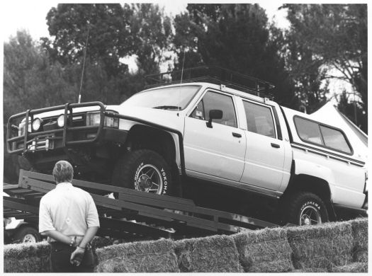 A man watching a 4 wheel drive vehicle being unloaded from a flat-bed truck at the Hall Show