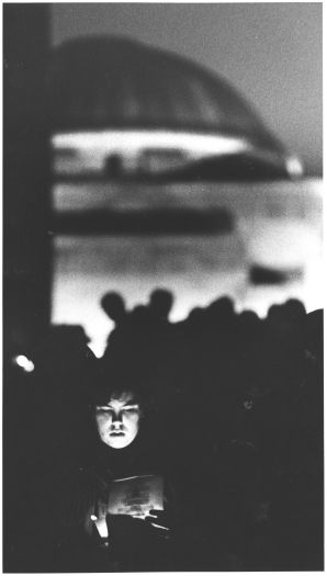 Dawn service at the Australian War Memorial. Shows a young person reading from a song book by torch light with the War Memorial lit up in the background.