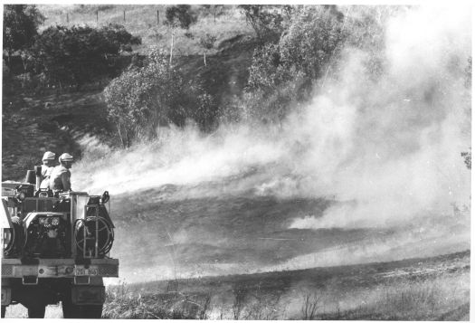 Grass fire in foothills adjoining Sulwood Drive being watched by fire crew from their truck