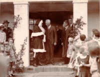 Photo shows a man shaking hands with Santa Claus and children lining the steps. Bertram Crosbie Goold can be seen on the right of the picture standing behind a man in an overcoat.