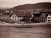 A front view of the Hotel Ainslie on the corner of Limestone and Ainslie Avenues. It shows the circular driveway to the entrance with Civic and Black Mountain in the distance.
