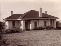 A front view of a typical Canberra house with flowers growing close to the house. The front yard is mostly lawn. The location is unknown.