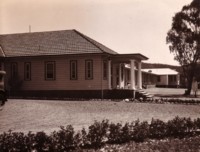 A side view of the Federal Capital Commission offices. It is a weatherboard building with a tiled roof. A rock-edged garden is also visible.