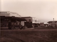 A car parked in front of Cusack's of Manuka on the corner of Flinders Way and Franklin Street and a sign above a butcher's stating "Pioneer Butcher Shop".