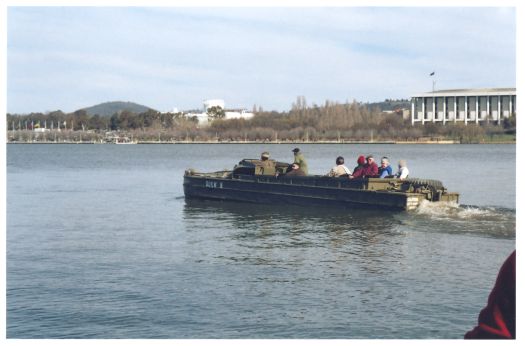 People riding on Lake Burley Griffin in an Army DUKW driven by a soldier. The National Library and Questacon are in the background.