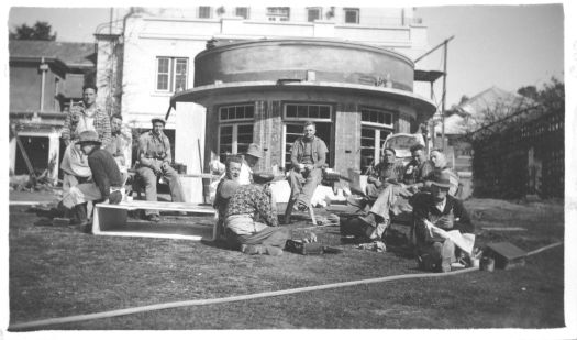 A group of workmen sitting in the sun eating lunch.