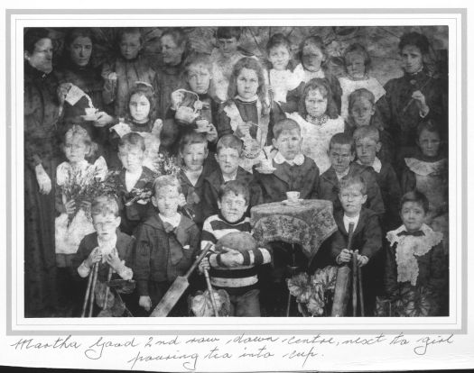 A young Martha Good in centre of second row, next to a girl pouring tea into a cup.

