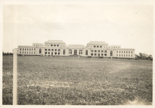 A distant view of Parliament House with two cars parked in front