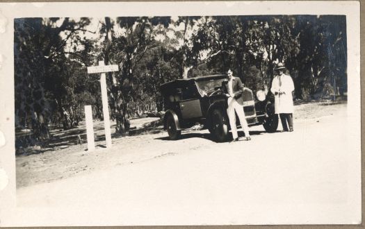 Two people standing besides a car with sign posts stating it was the boundary of NSW and the other that it was the Shire of Yarrowlumla