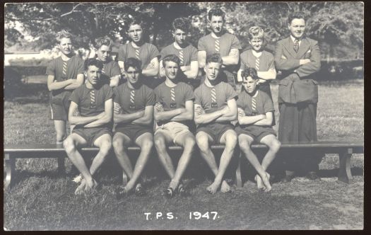 A team of eleven boys with their teacher - some standing, some sitting on a stool, some wearing boots