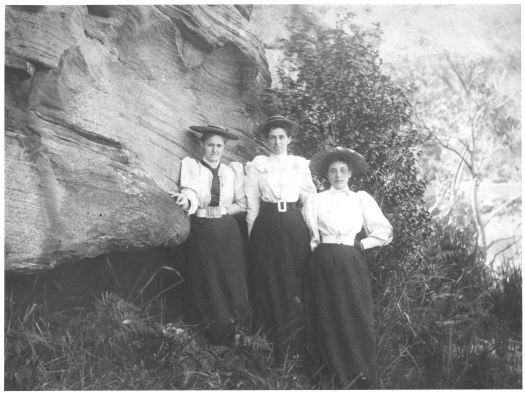 Picture of three young women standing next to a rock face: Hilda Robson (later Garran), Meg Garran and Mabel ? All three are wearing hats. 