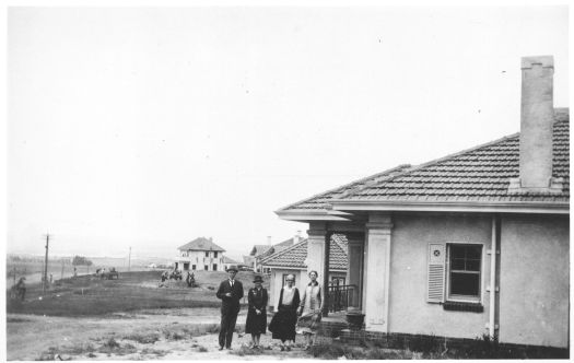 House at National Circuit, Blandfordia (now Forrest). View looking down the street to a two story house being built for Dr. Alcorn. A man and three women are standing in front of the house. The house was occupied by the Garrans in the 1920s while Roanoke was being built.