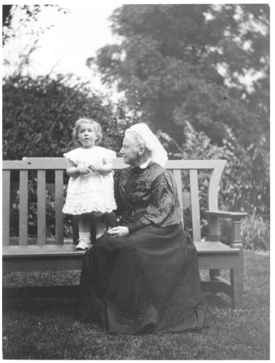 An elderly woman sitting on a garden bench looking at a young girl. Neither are identified.