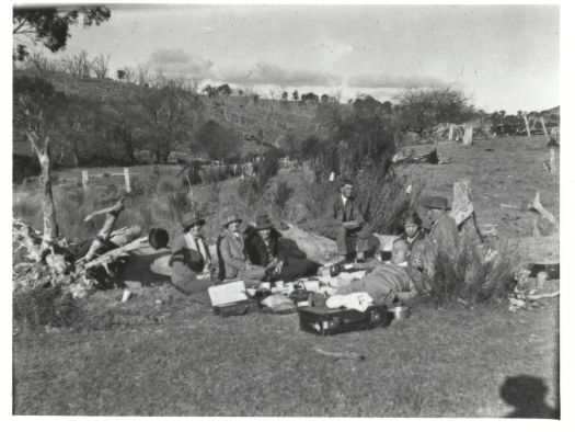Seven people at a picnic held in a paddock. All the men are wearing ties.