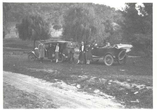 Two cars with seven unidentified people standing in front of the cars