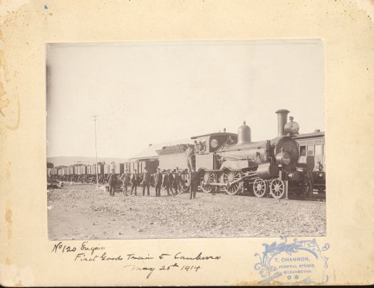 First goods train to Canberra. Shows train engine and carriages with three men on baord. Eight unidentified men are standing in front.