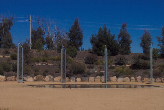 ACT Bushfire Memorial looking towards Cotter Road. Four tall glass tile columns stand behind a pond.