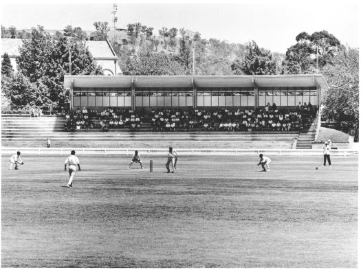 Cricket game at Manuka Oval with the newly built grandstand at the rear. St. Christopher's Cathedral is also visible.