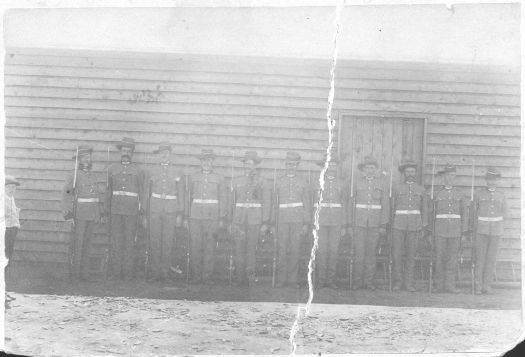 11 uniformed men of the Captains Flat militia standing to attention in front of a weatherboard building.